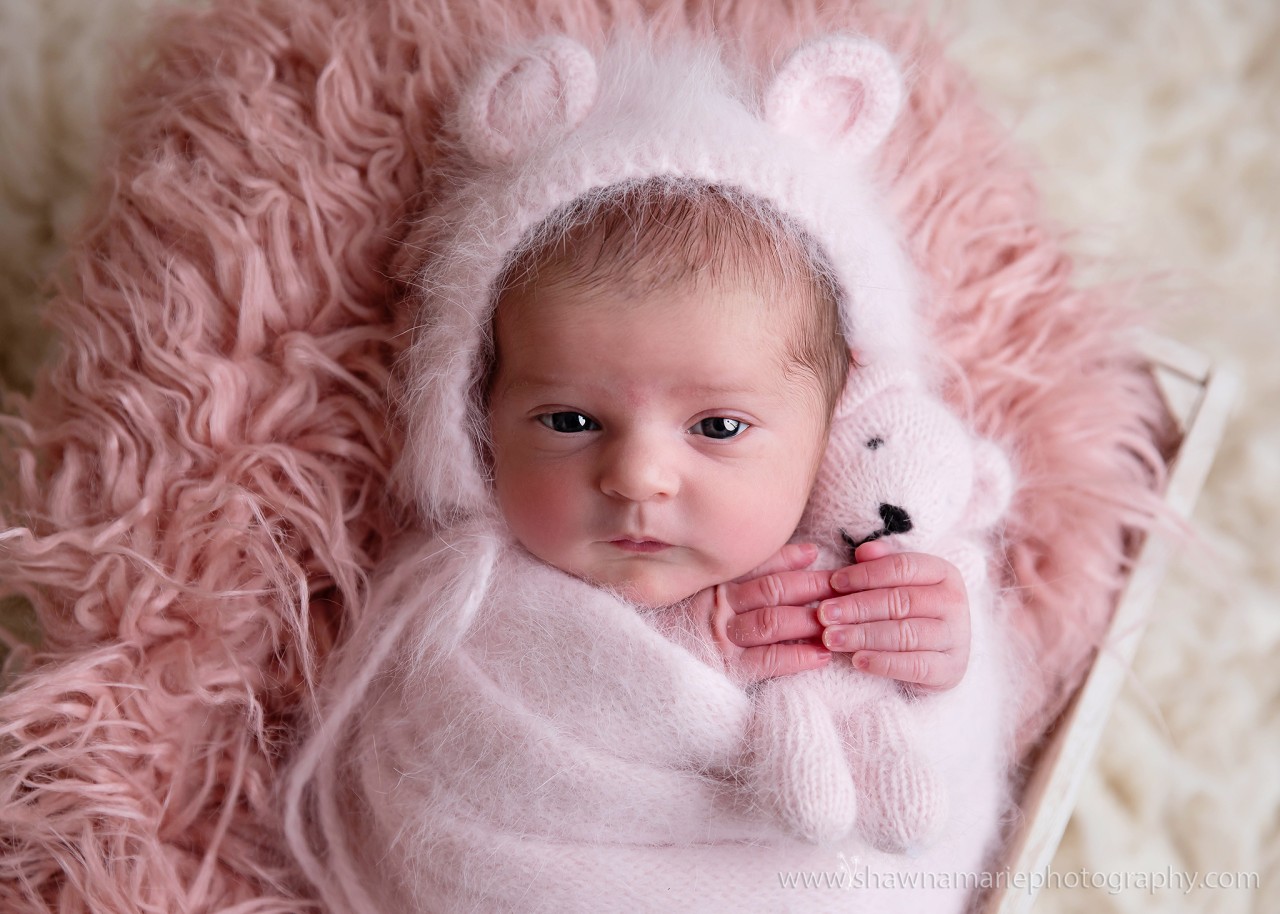 2 week old baby Alivia with eyes open wearing teddy bear hat and holding pink bear